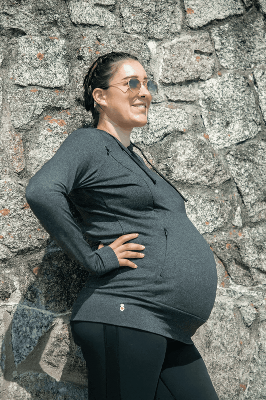 Pregnant woman wearing Luxe Maternity and Nursing Hoodie in charcoal marl, showcasing bump-friendly fit and breathable material outdoors.